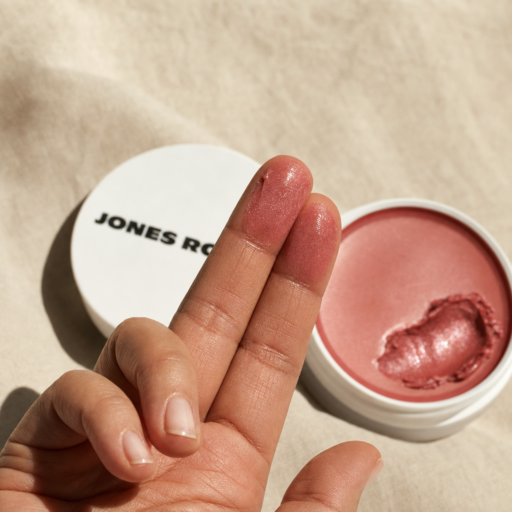 Macro close-up of fingertips warming the Dusty Rose Miracle Balm with the open pot beside them