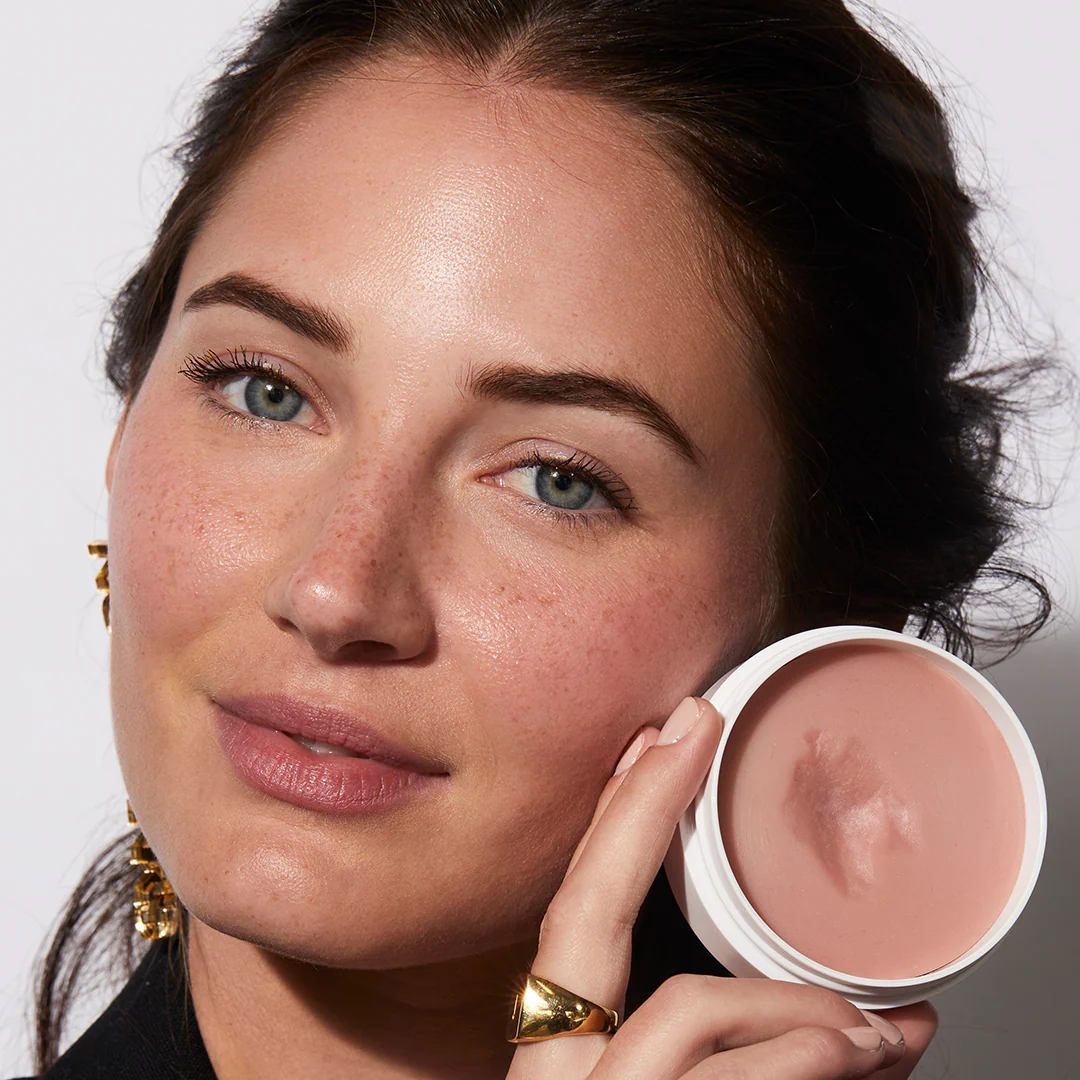 Woman with natural makeup holding the open Miracle Balm pot at her cheek