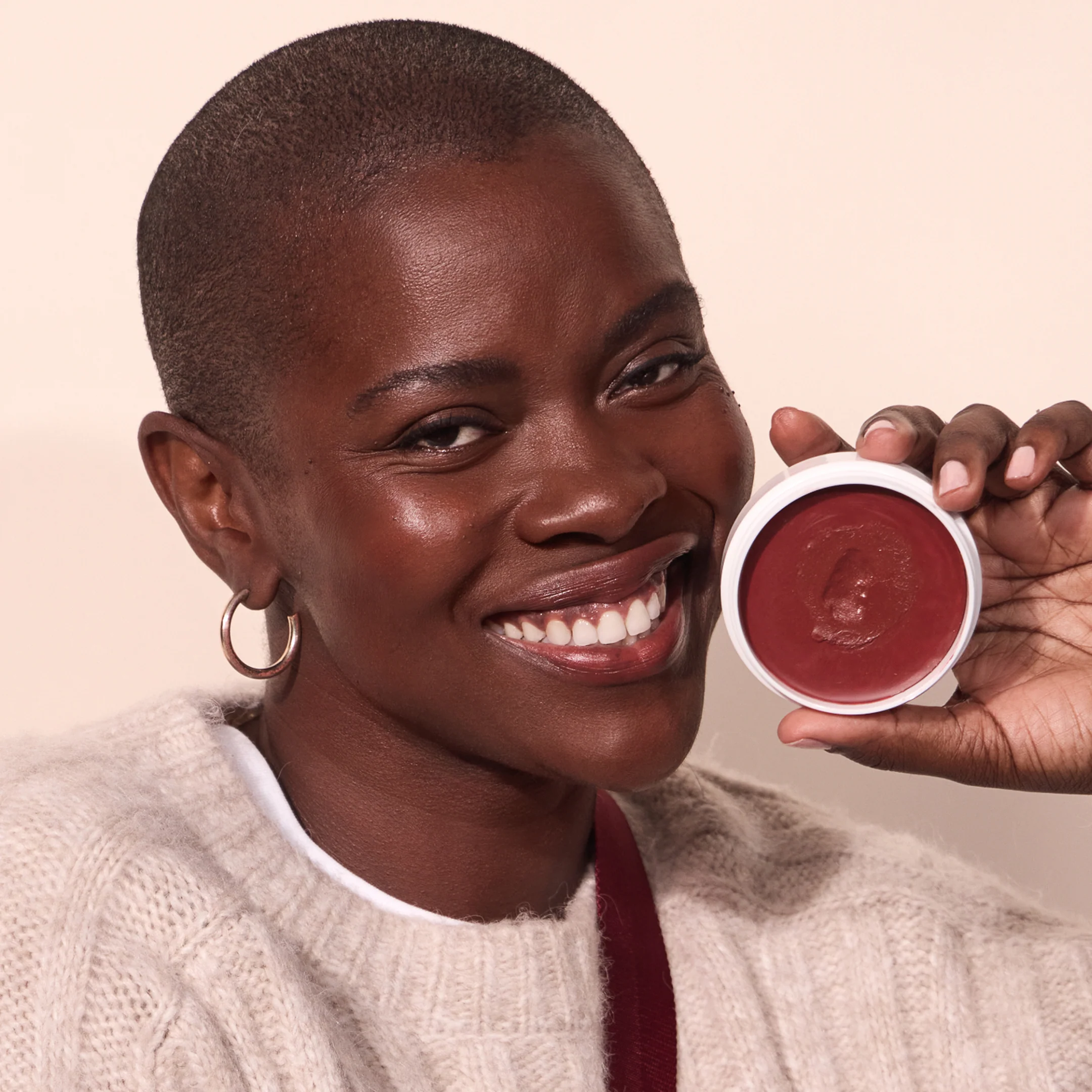 Woman holding Miracle Balm in Cheeky shade against her face